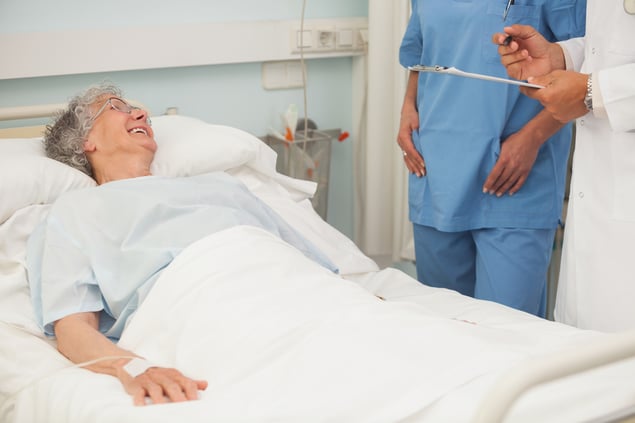 Elderly female patient smiling up at nurse and doctor from hospital bed